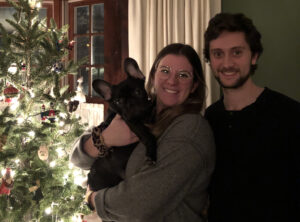 Couple in front of Christmas tree holding their dog.