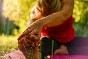 Person seated and stretching on yoga mat over one extended leg while other leg is bent.