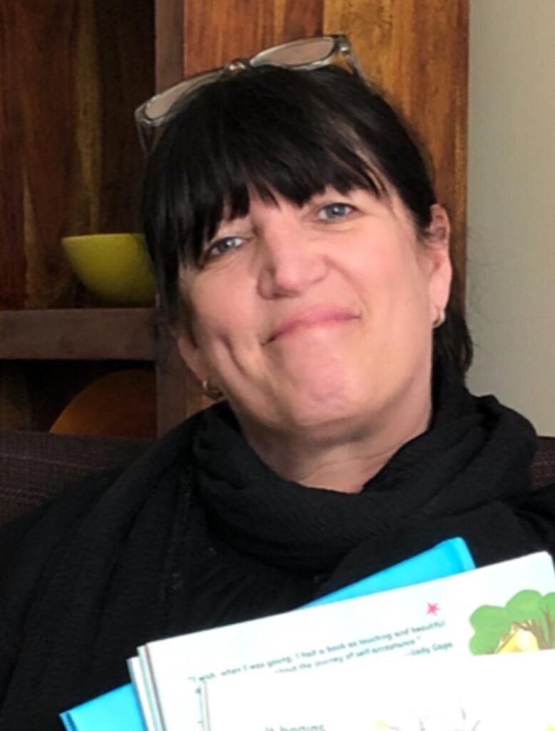 Tammy Moffatt casual headshot with glasses on top of her head, holding books.